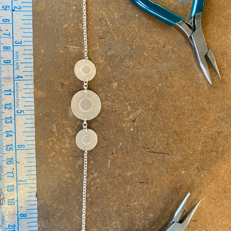 Jewellery making tool on a bench alongside a ruler and a silver necklace